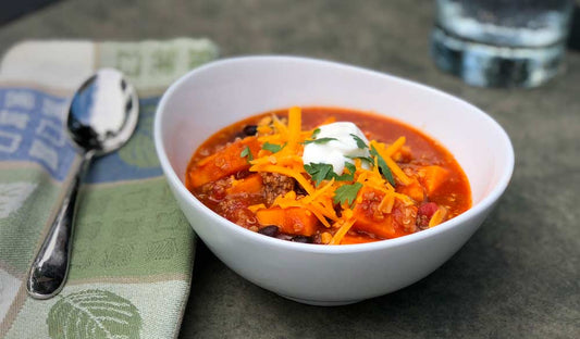 Bowl of sweet potato and quinoa chili topped with avocado and cilantro